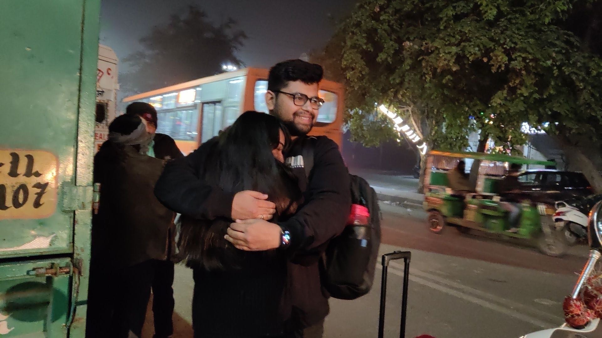 Rajat and Ishika sharing a tight hug at night beside a bus, luggage at their feet