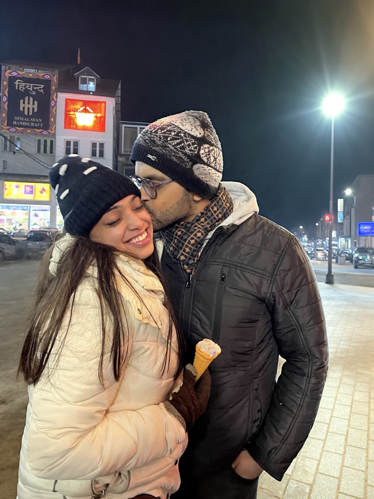 Rajat kissing Ishika's cheek on a cold night in Manali, both in beanies and jackets, holding ice cream