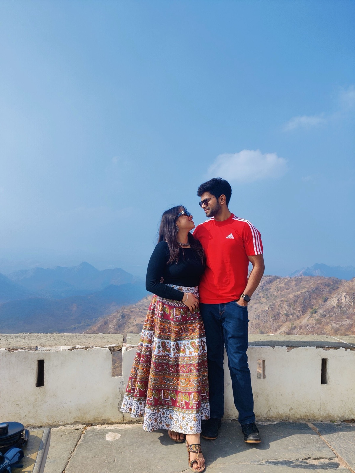 Rajat and Ishika gazing at each other on a hilltop wall in Udaipur, mountains behind them