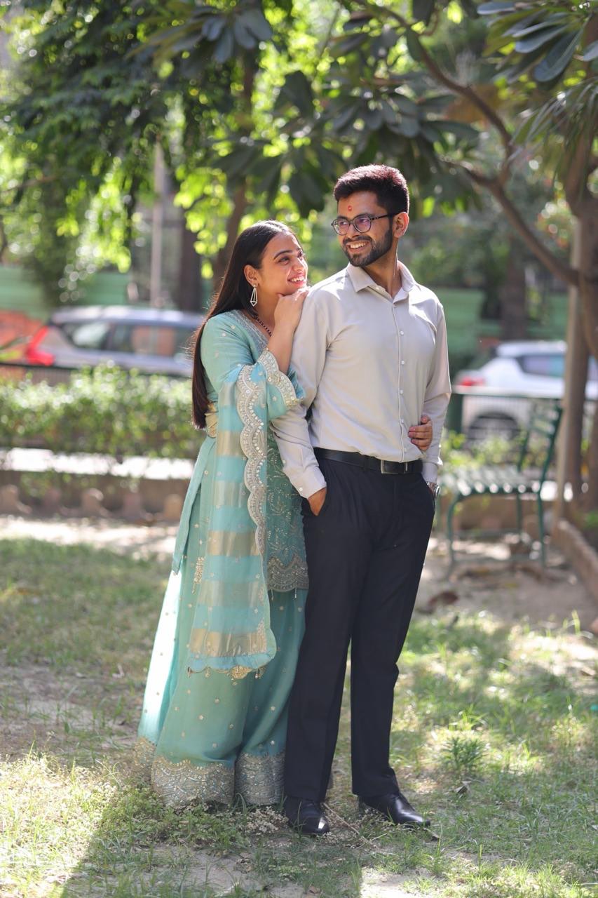 Ishika in a mint embroidered suit leaning on Rajat in a cream shirt, under dappled trees