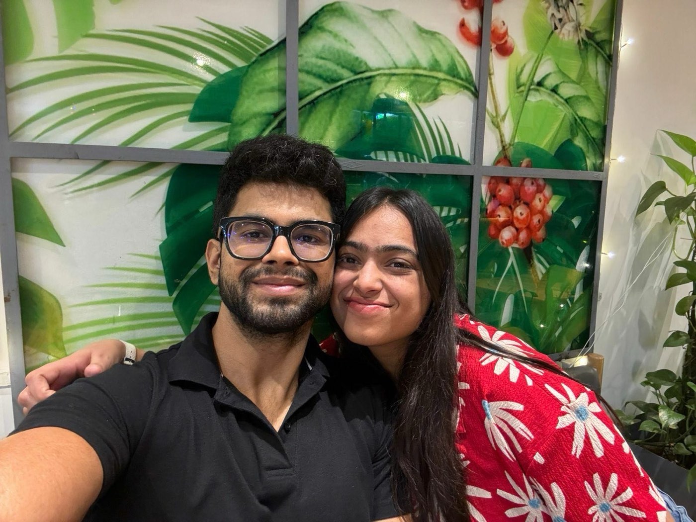 Rajat and Ishika side by side in a cafe in the evening, Ishika in a red floral top